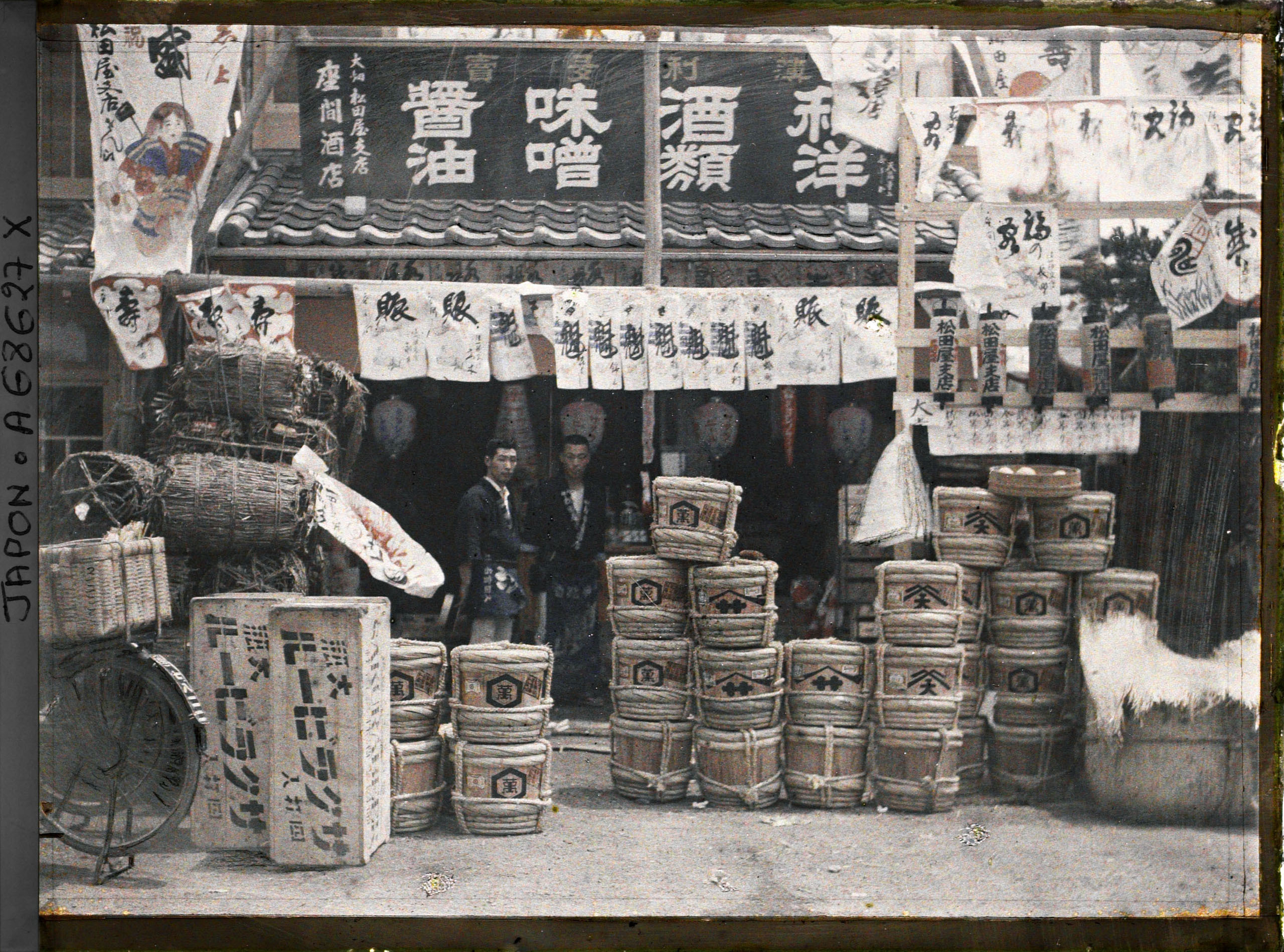 Grocers at the entrance of a shop in Tokyo with barrels of beer, miso, sake and charcoal on display, photographed by Roger Dumas, 1926–1927.